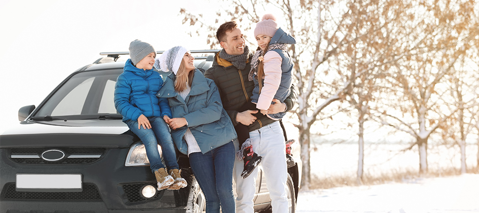smiling family in front of car on winter road